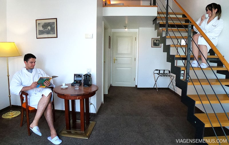Hotel romântico em Praga: quarto de baixo, um sentado na mesa tomando café, outra sentada na escada, os dois de roupão e pantufas