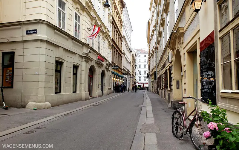 Museus em Viena - uma rua tranquila no centro antigo de Viena, rua estreita, prédios amarelado do século 19, uma bicicleta e flores no canto direito.