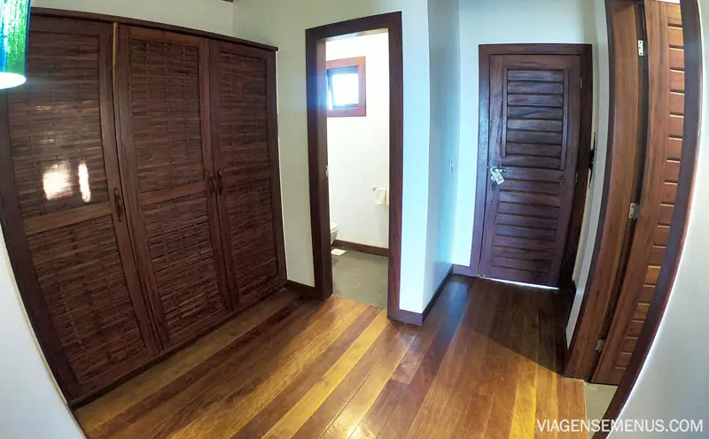 Espaço entre os dois banheiro, piso de madeira e guarda-roupa de madeira escura