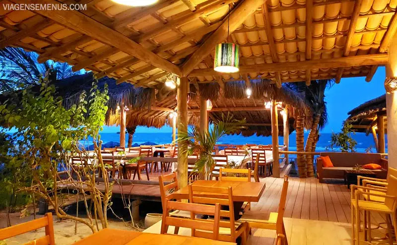 Hotel Vila Selvagem, Fortim, Ceará - vista panorâmica do restaurante à noite, iluminado, mesas e cadeiras de madeira, luminária praiana verde