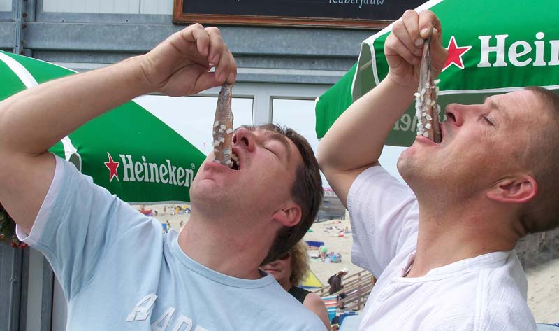 O que comer em Amsterdam - Haring, peixe Arenque. Imagem de dois holandeses comendo o peixe.