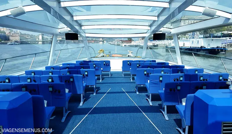 Passeio de barco em Budapeste - barco com cadeiras azuis e laterais e teto de vidro 