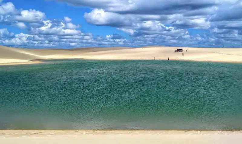 Grande lagoa esverdeada com carro 4x4 ao fundo e pessoas tomando banho - Lençois Cearenses Caetanos Ceará