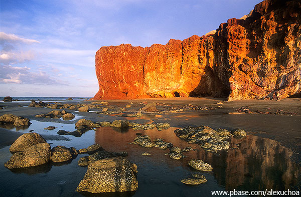 Praia da Redonda com falésia alaranjada ao fundo e várias pedras pequenas na areia - Icapuí, Ceará